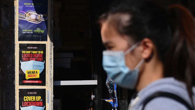 woman wearing a surgical mask, with "wear a mask!" poster in background