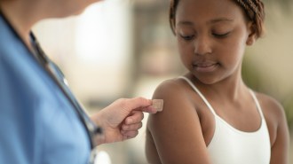 a little Black girl getting a peach-tented bandaid from a nurse