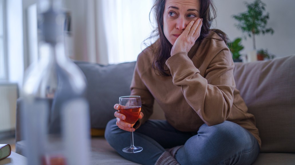 distraught woman sitting on a sofa with a glass of wine