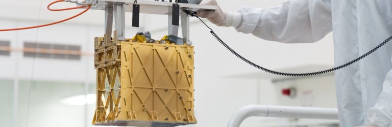 a person in a clean suit maneuvers a gold-colored cube