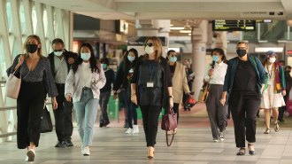 masked people walking in a train station overpass tunnel