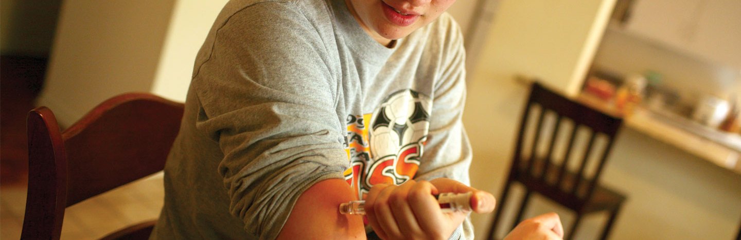 A young woman sitting at a kitchen table injects insulin into her arm