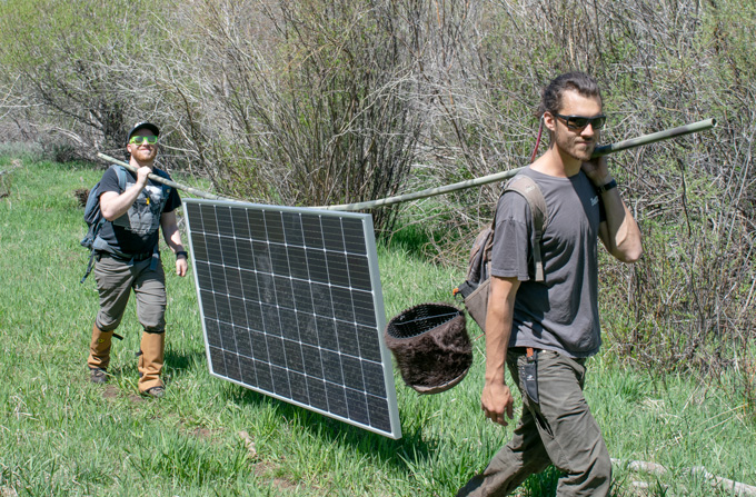 two ecologists carry solar panels in the field