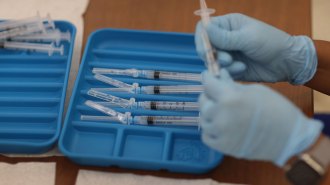 Moderna COVID-19 vaccines being prepared in syringes, held by a person wearing blue gloves
