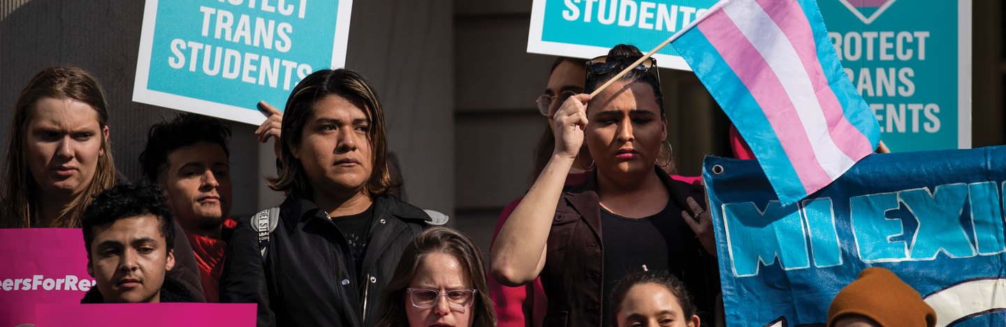 people hold posters and flags in support of transgender people