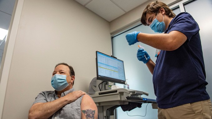 Mark Turney rolls up his sleeve to receive a booster shot