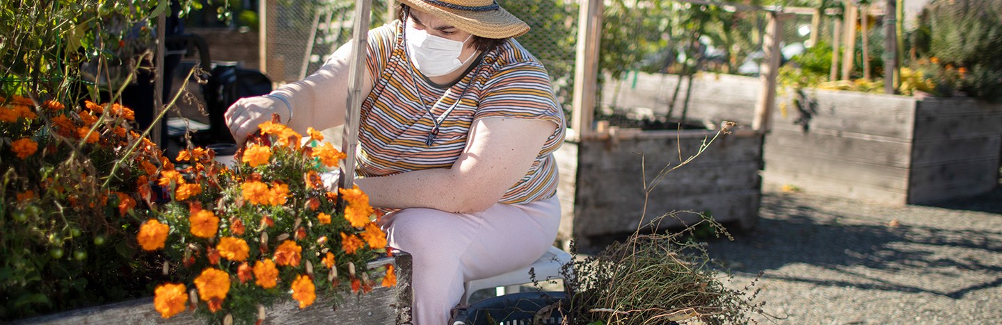 woman wearing face mask and hat tending to flowers in garden