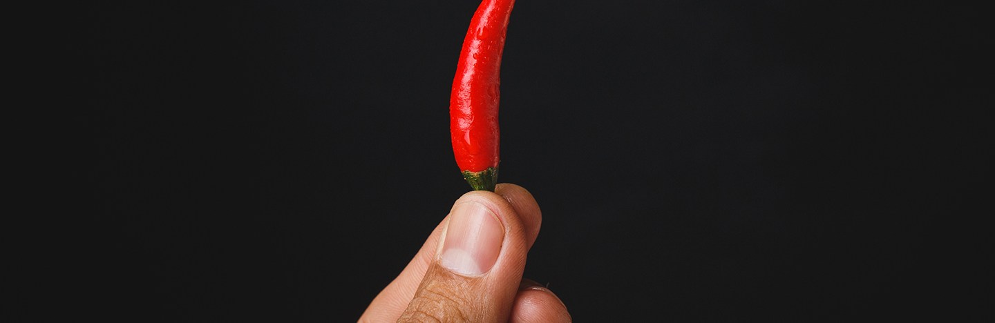 a person holding a small red chili pepper with their fingertips