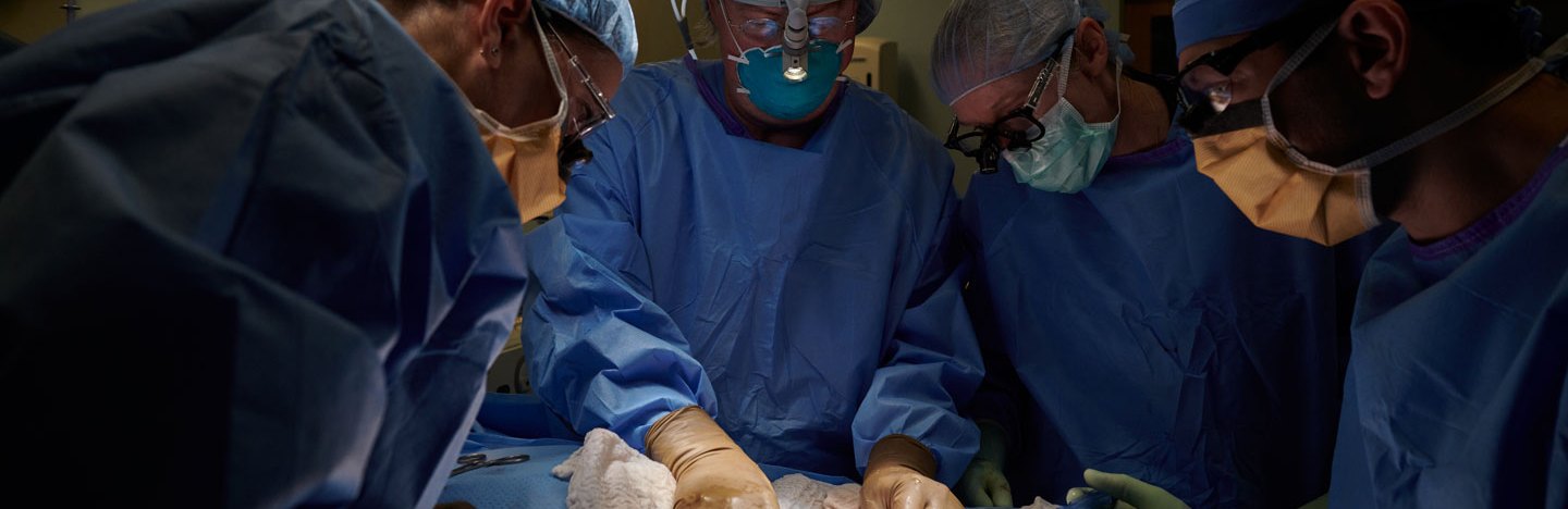 several doctors in scrubs and masks look at a patient on an operating table