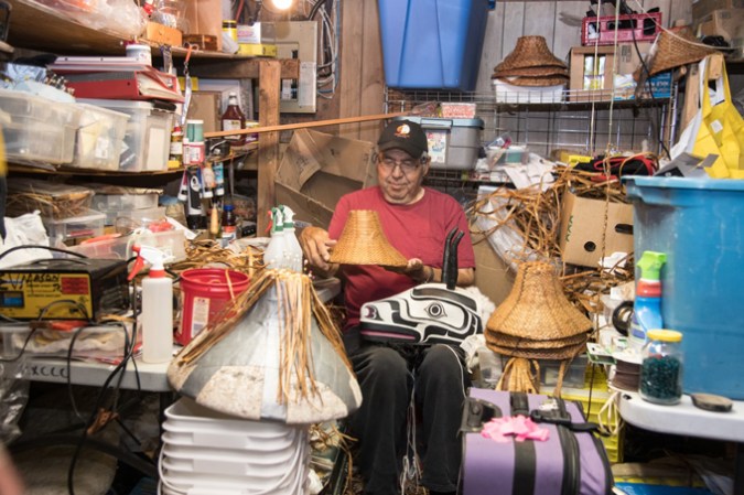 photo of Ernest V. Mason sitting in a storage room with a black and white carved mountain goat mask on his lap