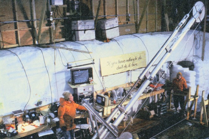 photo of ice core drilling set-up with one scientist by the drill and another scientist in the background