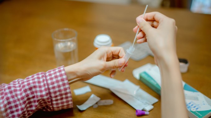 pov image of someone dipping a nasal swap into a covid test tube