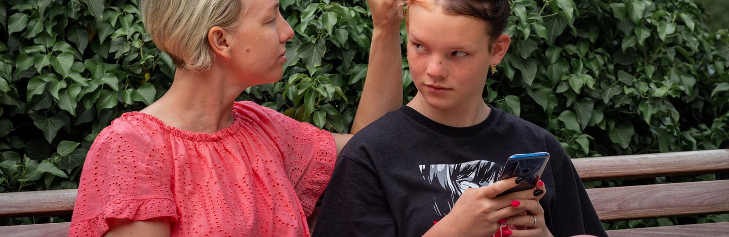 a mom looking at her daughter, who is looking annoyed while holding a phone