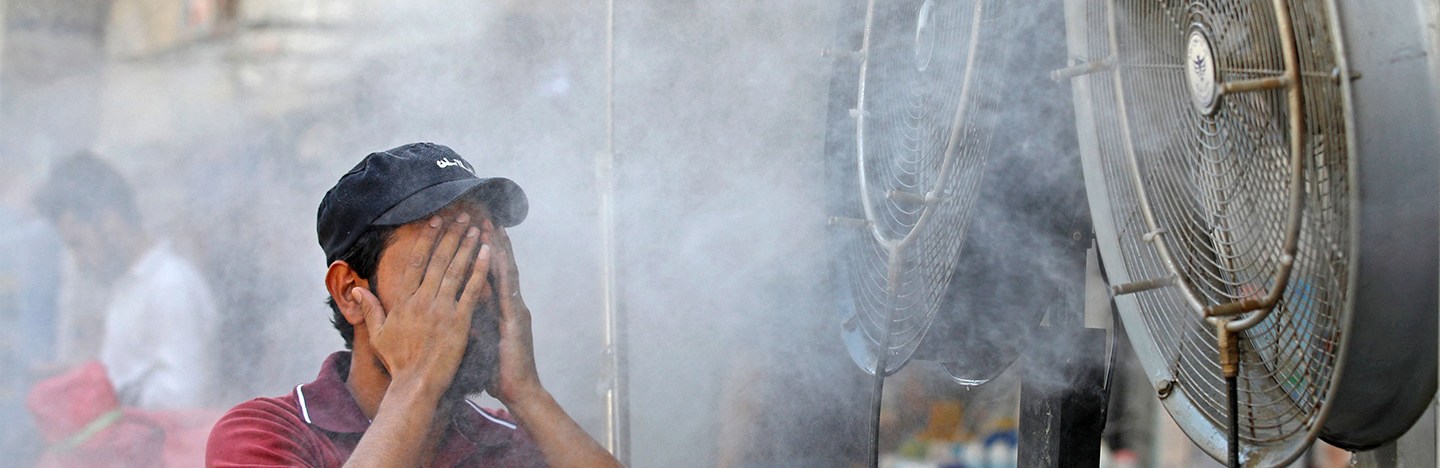 a man in a red shirt and a black cap standing in front of a misting fan