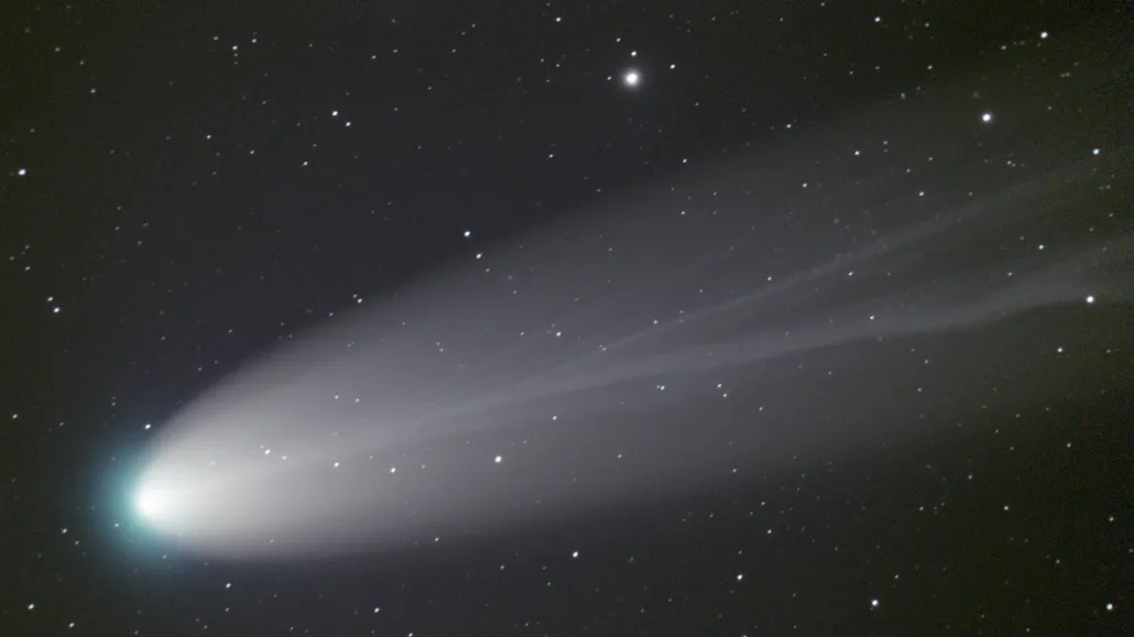 Comet Leonard streaking across the night sky, with a greenish tinge at its head