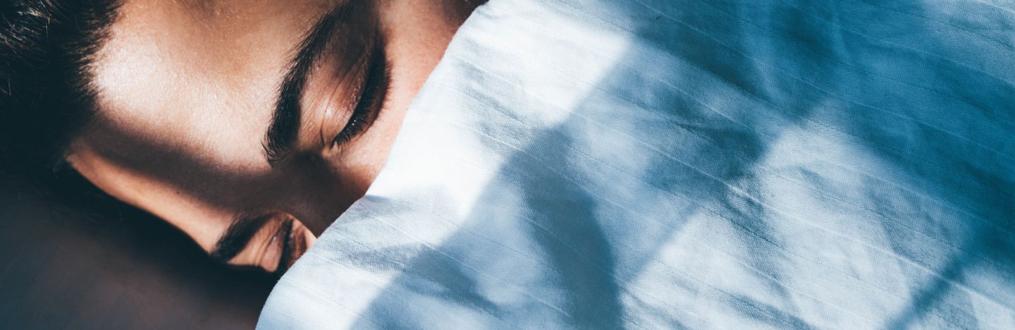 image of the face of someone sleeping in bed under a blue sheet