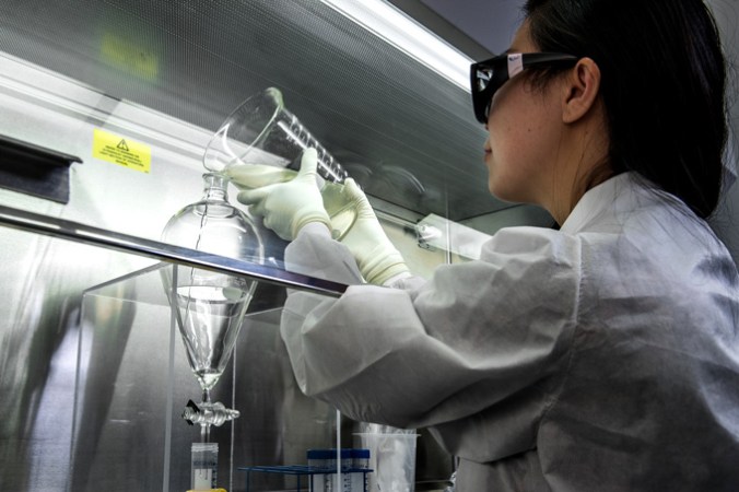 photo of a scientist pouring a wastewater sample from a beaker into separatory funnel in a fume hood