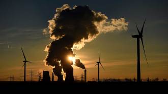 Wind turbines stand near a coal-fired power plant in Germany, with steam rising from the plant's cooling towers.
