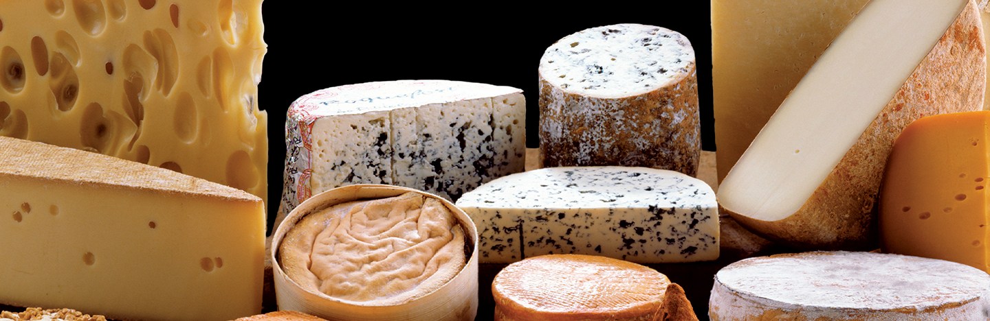 A collection of different cheeses stacked in a pile with a black background.