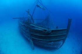 An underwater photo of a replica sunken merchant ship with a scuba diver swimming above.