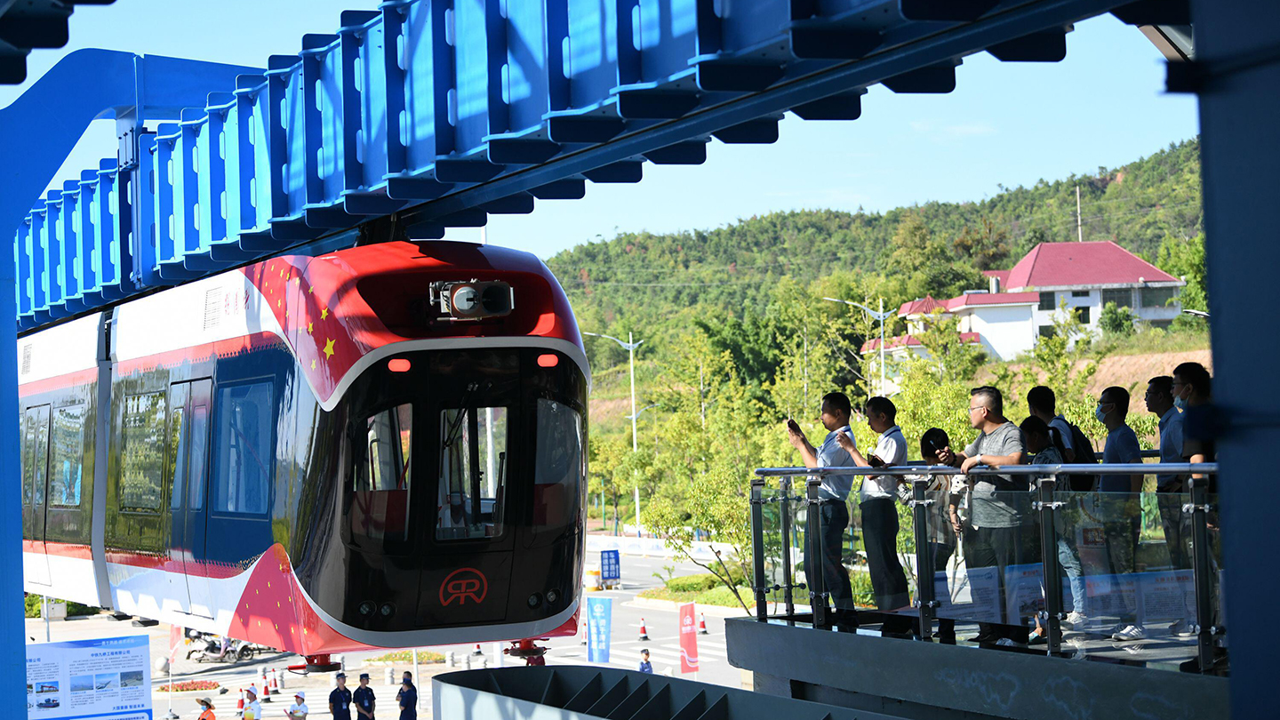 A photo of China's maglev train as it comes into a station with several people standing at balcony of a nearby platform.