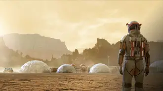 An astronaut in a space suit stands with their back to the camera and looks out at inflatable domes as part of a habitat on Mars.