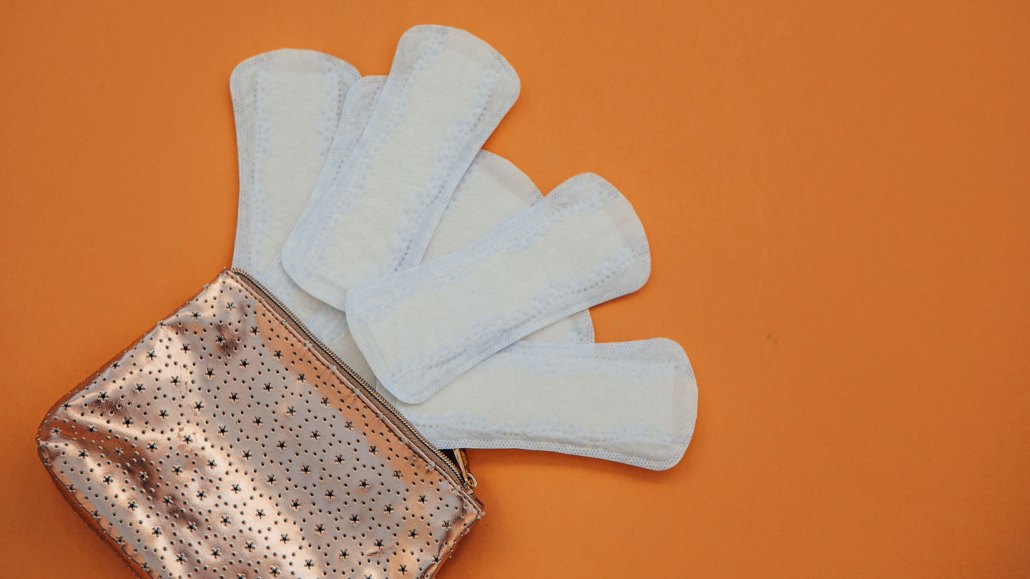 A photo of several maxi pads spread out of a small bag on an orange background.