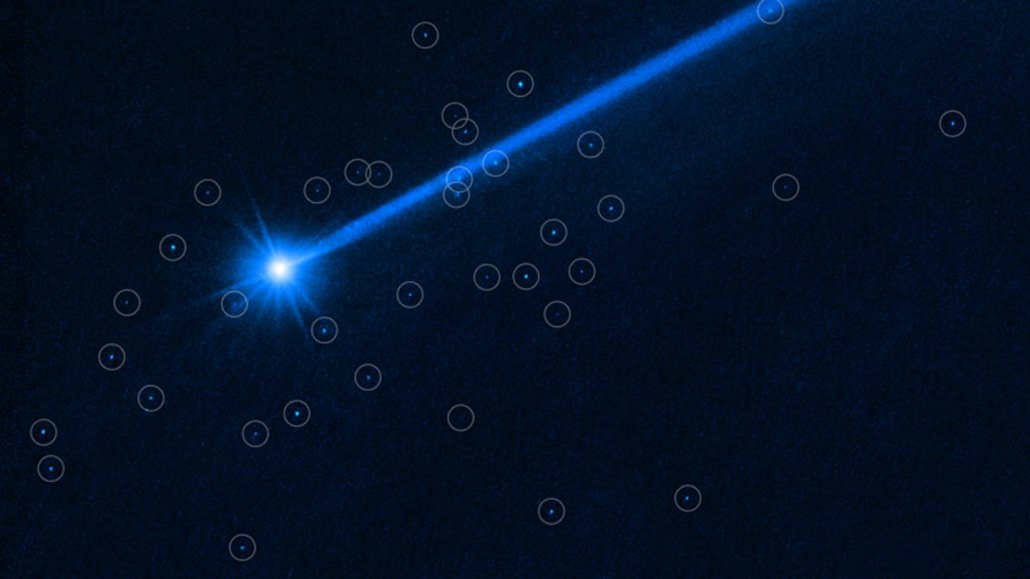 Hubble telescope image showing a blue trail of dust behind the asteroid Dimorphos (also blue), with circles showing new boulders around the asteroid