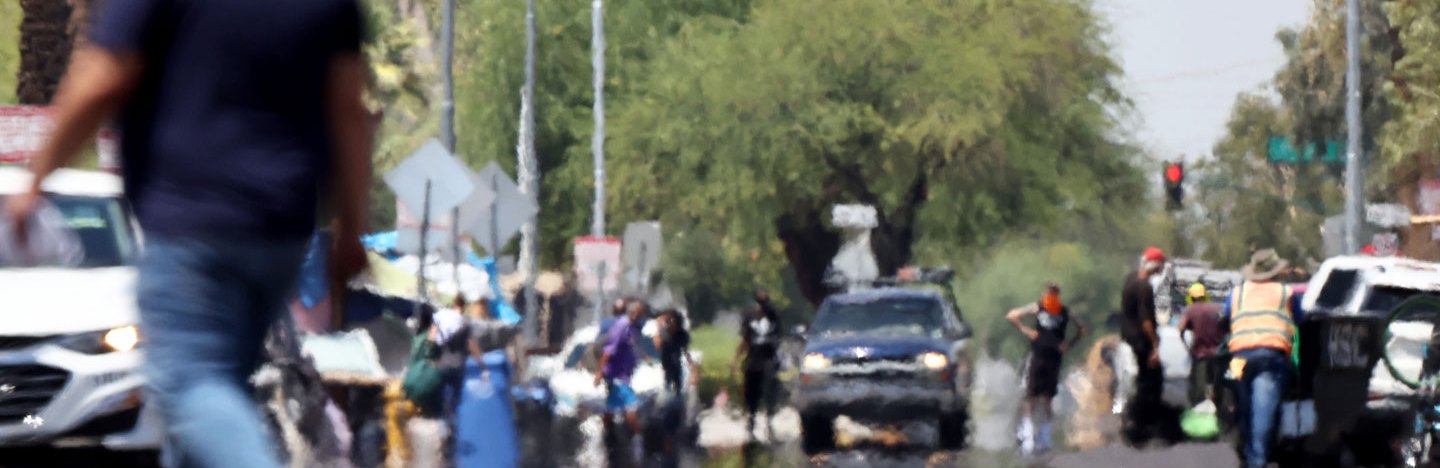 A photo of a busy street with people walking around and cars on the road. Heat haze can be seen on the road.