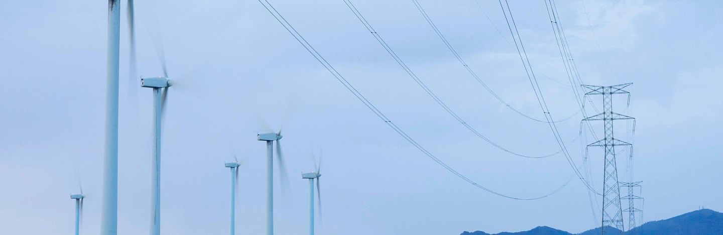 A photo of wind turbines in a grassy area with power lines nearby.