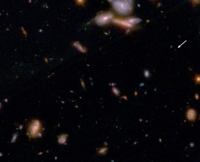 An image taken by JWST shows a tiny dot of light, indicated with an arrow, amid a section of sky scattered with galaxies.