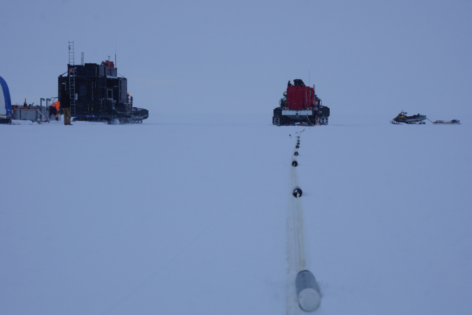 A photo showing a tractorlike vehicle pull a daisy-chain of seismometers across the ice.