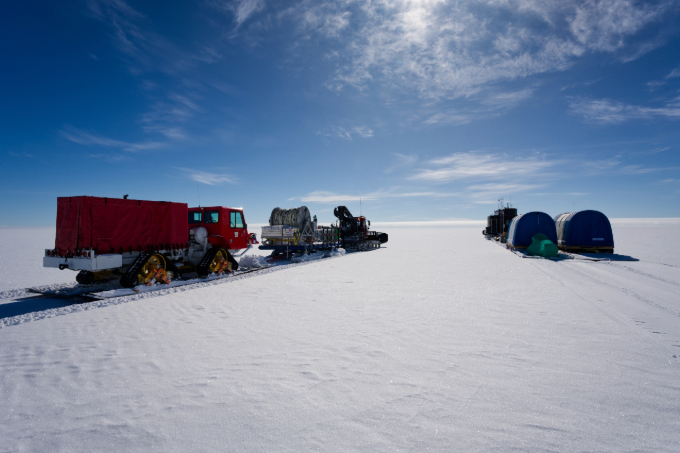 Two tractorlike vehicles drive on a field of ice.