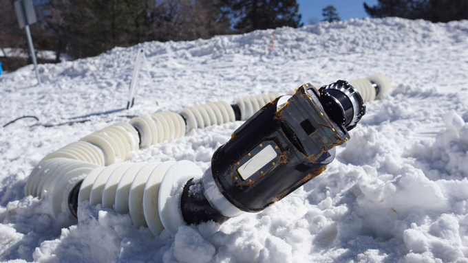 A photo of a snakelike robot, known as NASA's Exobiology Extant Life Surveyor, resting on the snow.