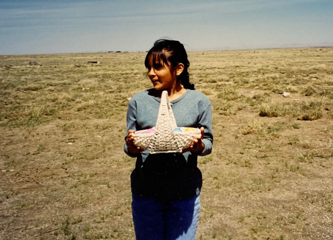 A photograph of Krystal Tsosie as a child standing in field on the Navajo Reservation in Leupp, Ariz. She's holding a white basket with plastic Easter eggs in it.