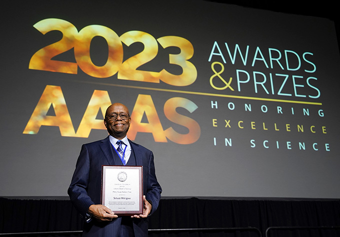 Sekazi Mtingwa holds a plaque in front of a screen that reads "2023 AAAS Awards & Prizes honoring excellence in science"