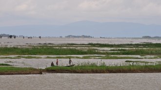 Three people on a boat look at the Ganges River with mountains in the background