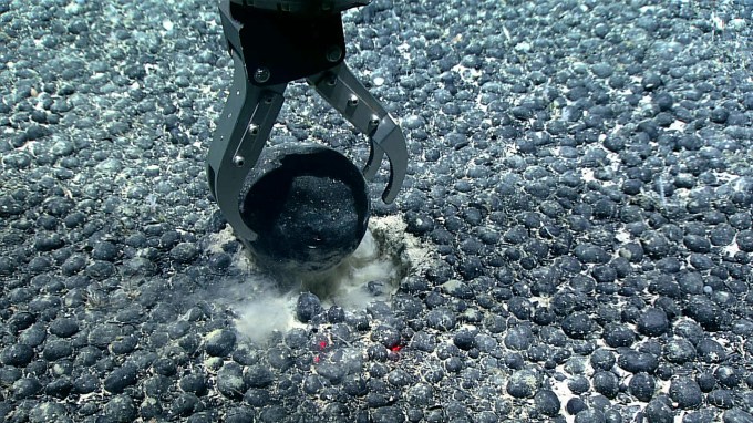 A metal claw reaches for a round nodule on the seafloor.