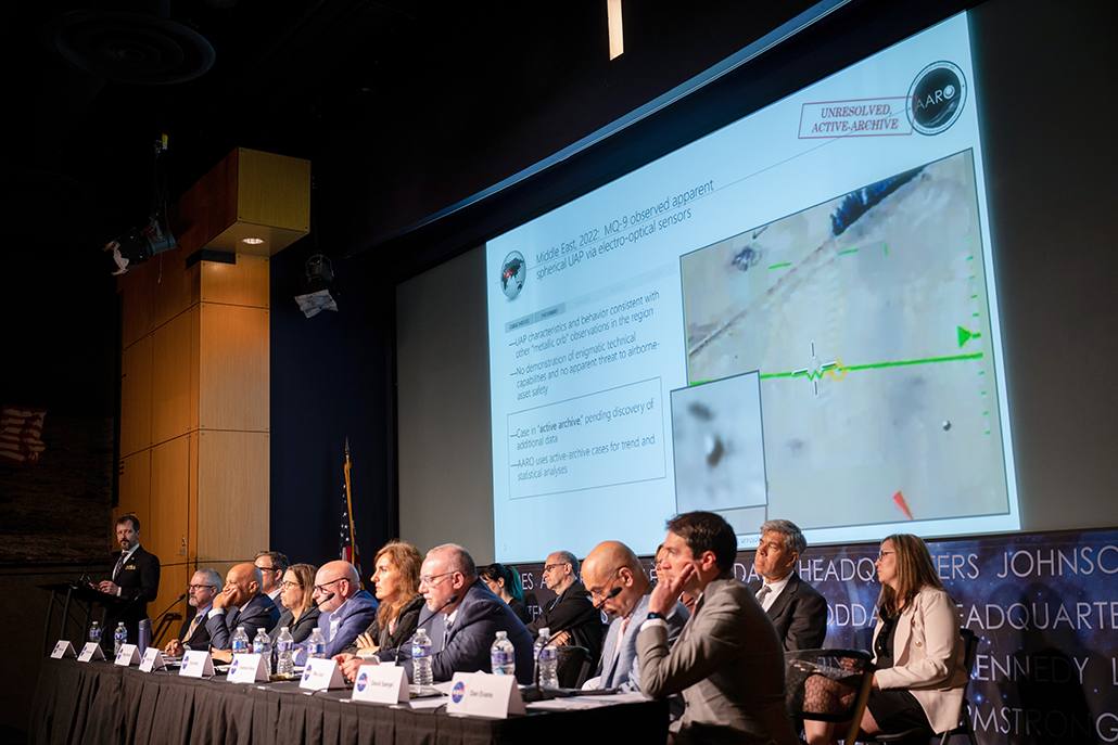 a group of experts sitting at a panel table with a projection behind them
