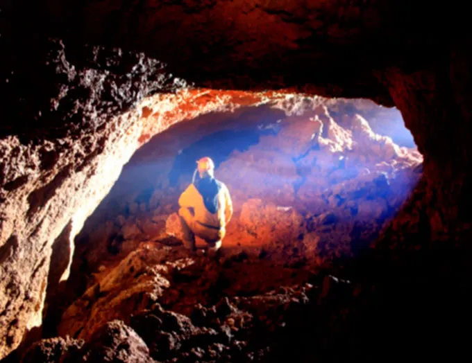 A person sits in a cave opening.