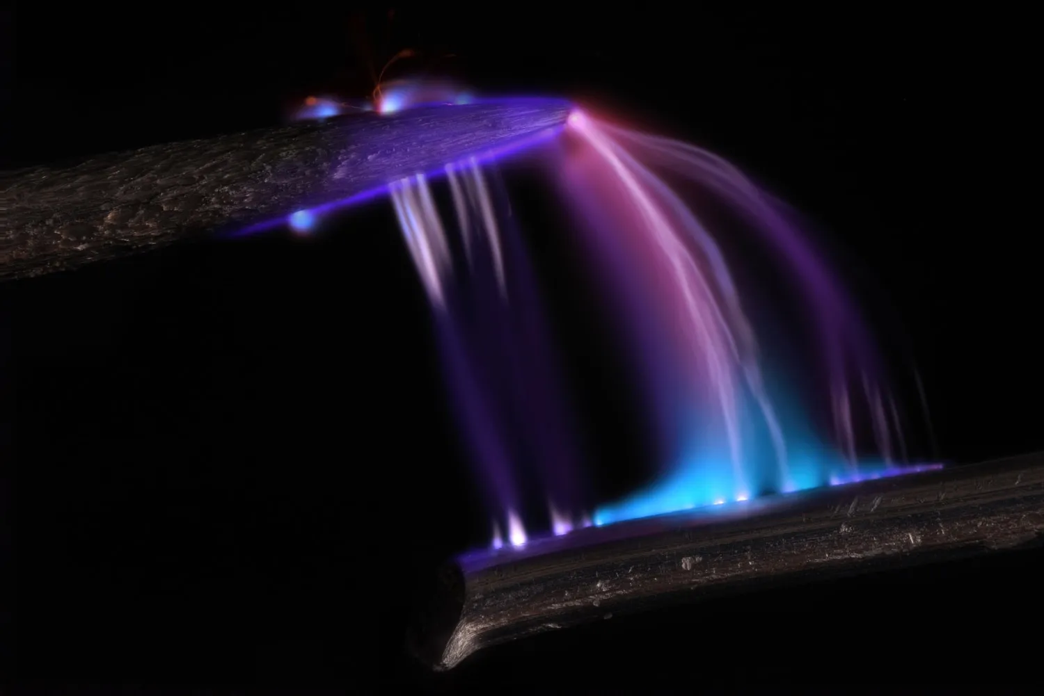 Multicolored arcs of light stream down from the highly magnified tip of a pin to a dark surface