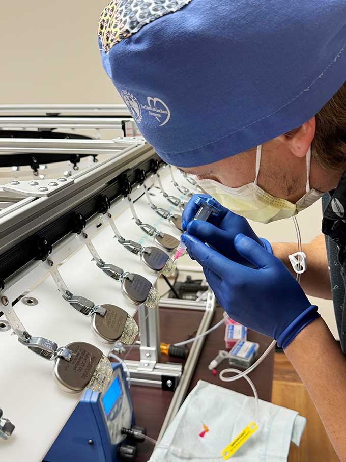 A doctor peers over a line of about a dozen pacemakers  as he cleans one with solution from a syringe