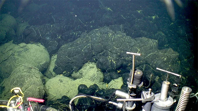 Silver machinery sits against a collection of large lava rocks in an underwater ocean photo