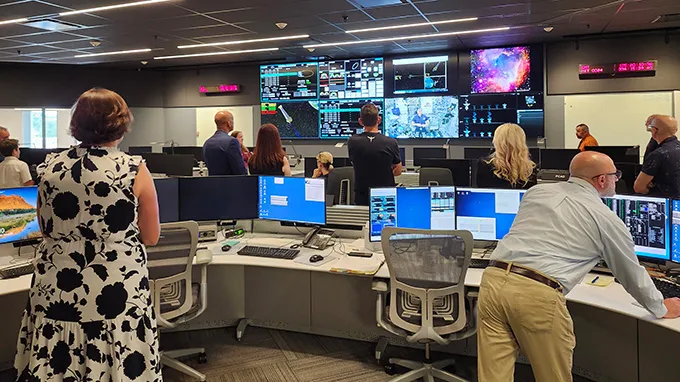 A bunch of people in a control room are looking at a set of screens mounted on a wall showing images and date related to the Chandra X-ray telescope.