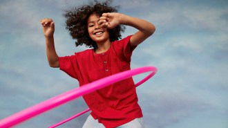A smiling child swings a pink Hula-Hoop around their waist.