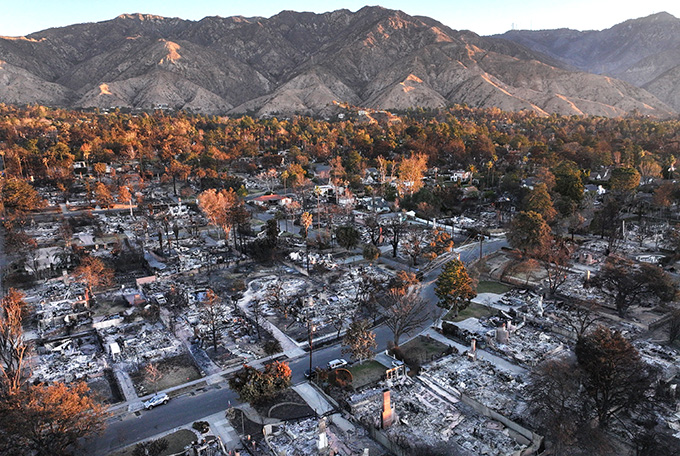 A razed neighborhood is in the foreground, with charred mountains in the background.