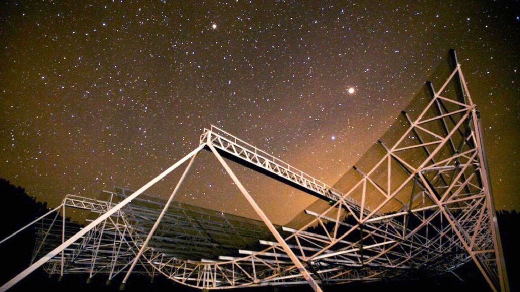 A large radio dish sits beneath a starry sky.