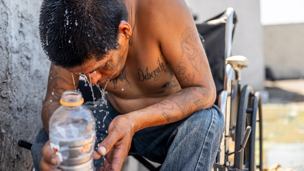A seated man splashes water from a bottle on his face