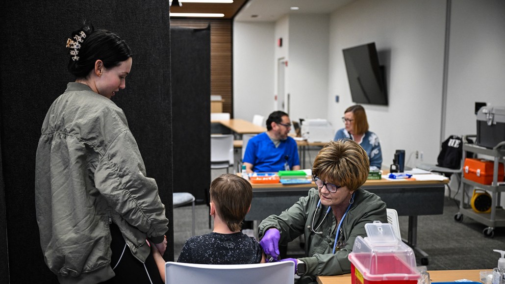 A health care worker administers a measles vaccine to a child while a family member holds his other hand.