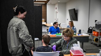 A health care worker administers a measles vaccine to a child while a family member holds his other hand.